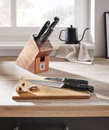 Messerblock Spitzenklasse 6-teilig auf einer Küchenarbeitsplatte, mit zwei Messern auf einem Schneidebrett im Vordergrund, seitliche Perspektive.