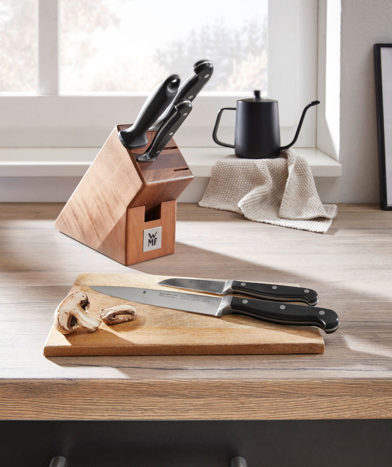 Messerblock Spitzenklasse 6-teilig auf einer Küchenarbeitsplatte, mit zwei Messern auf einem Schneidebrett im Vordergrund, seitliche Perspektive.