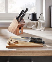 Messerblock Spitzenklasse 6-teilig auf einer Küchenarbeitsplatte, mit zwei Messern auf einem Schneidebrett im Vordergrund, seitliche Perspektive.