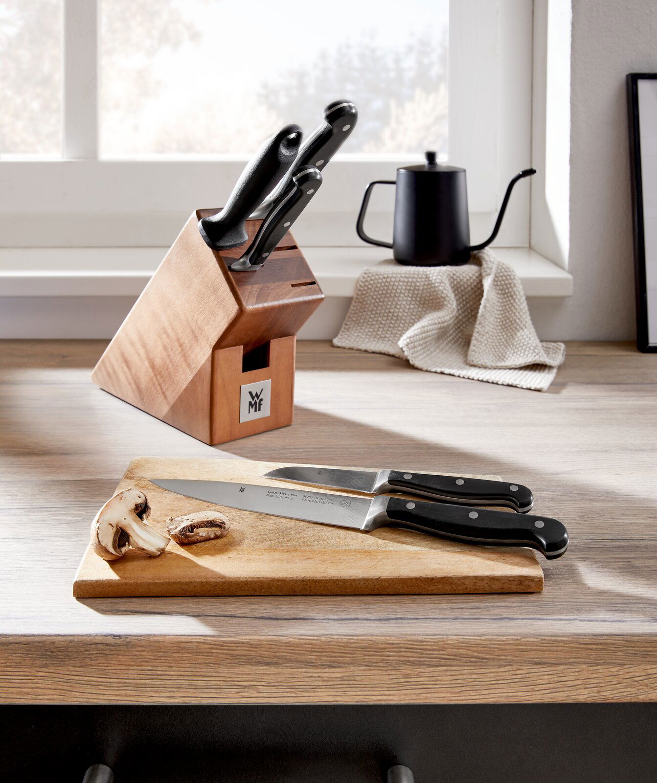 Messerblock Spitzenklasse 6-teilig auf einer Küchenarbeitsplatte, mit zwei Messern auf einem Schneidebrett im Vordergrund, seitliche Perspektive.