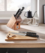 Messerblock Spitzenklasse 6-teilig auf einer Küchenarbeitsplatte, mit zwei Messern auf einem Schneidebrett im Vordergrund, seitliche Perspektive.