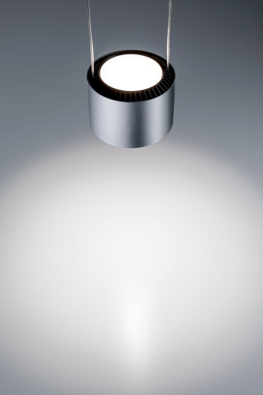 Moderne, zylindrische Hängeleuchte in silberner Farbe, von oben fotografiert, mit hellem Lichtstrahl auf einer grauen Oberfläche.