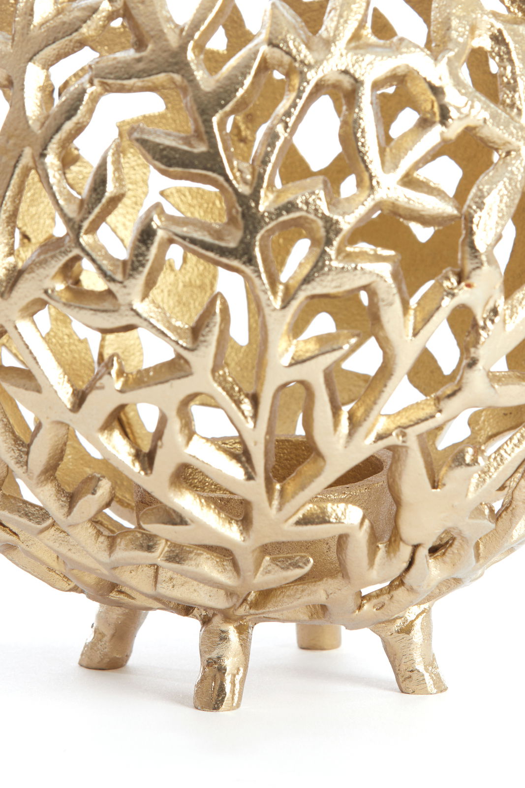 Nahaufnahme eines goldenen Teelichthalters mit filigranem, blattähnlichem Muster und kleinen Füßen, seitliche Perspektive.