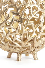 Nahaufnahme eines goldenen Teelichthalters mit filigranem, blattähnlichem Muster und kleinen Füßen, seitliche Perspektive.