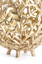 Close-up van een gouden theelichthouder met een filigraan, bladachtig patroon en kleine voetjes, gezien vanaf de zijkant.