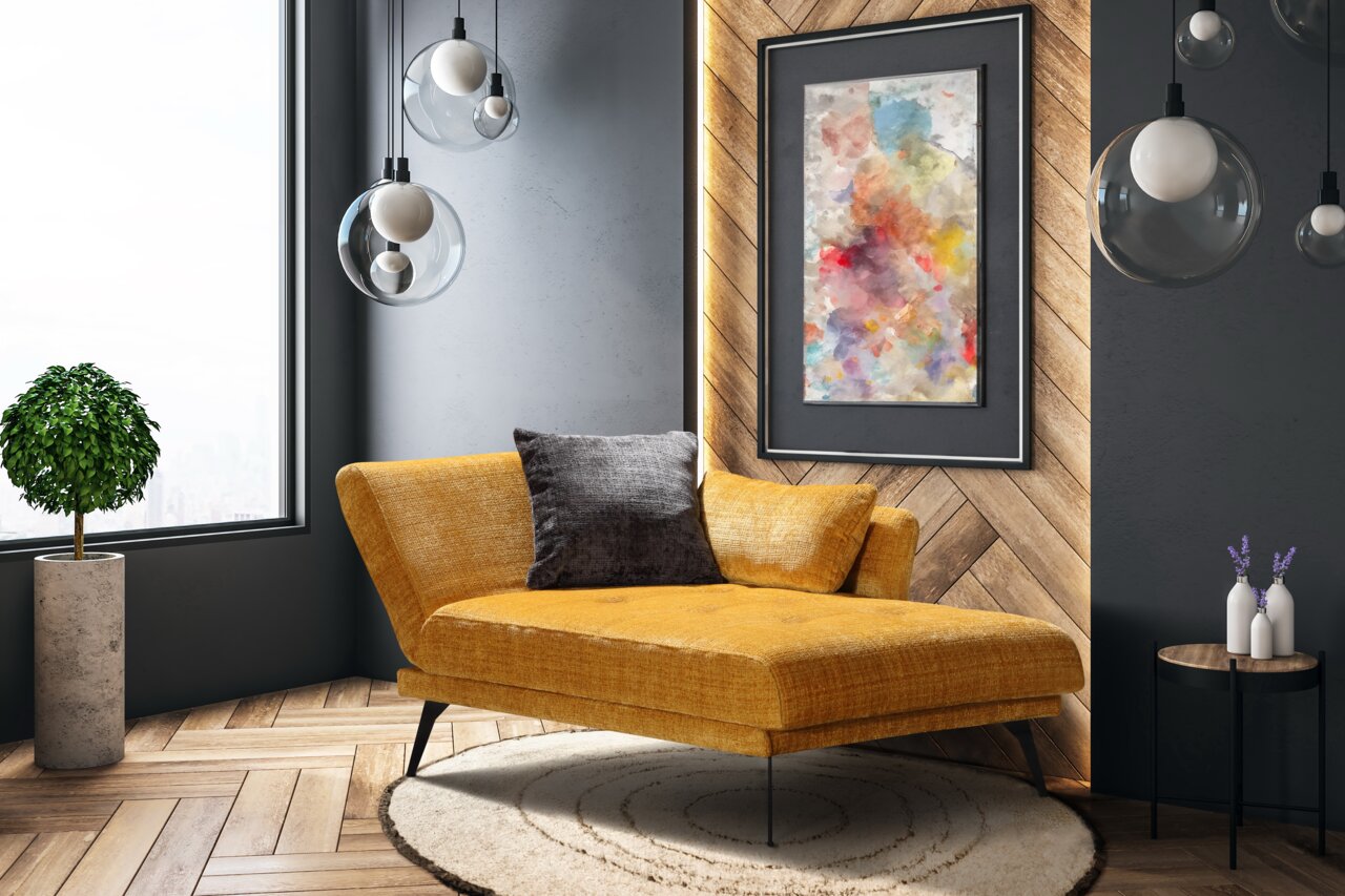 Gezellige eenpersoonsligstoel in mosterdgeel met een zwart kussen, gezien vanaf de zijkant, in een moderne woonkamer met een houten visgraatvloer, hangende glazen bolvormige lampen en een abstract wandschilderij.