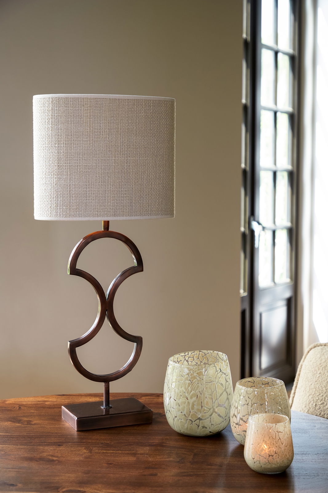 Moderner Tischlampenschirm in ovaler Form mit elegantem, geschwungenem Metallfuß, frontal auf einem Holztisch platziert.