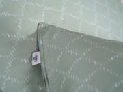 Nahaufnahme einer Bettwäsche in sanftem Grün mit dezentem Muster und sichtbarem Etikett, Perspektive von oben.