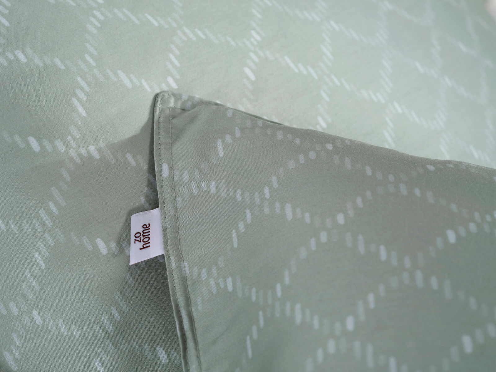Nahaufnahme einer Bettwäsche in sanftem Grün mit dezentem Muster und sichtbarem Etikett, Perspektive von oben.