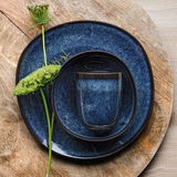 Blauer Frühstücksteller Lave 23,5 cm mit passendem Becher und dekorativer Blume, von oben fotografiert.