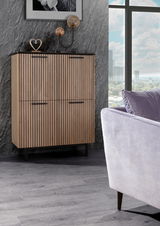 Modernes Highboard mit vertikalen Holzlamellen, seitliche Perspektive, dekoriert mit Skulpturen und Lampen, vor einer grauen Wand.