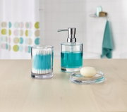 Transparentes Bad-Accessoire-Set aus Glas: Seifenspender mit türkisfarbener Flüssigseife, Wattestäbchen-Behälter und Seifenschale mit Seifenstück, frontal aus leicht erhöhter Perspektive auf einem hellen Waschtisch.