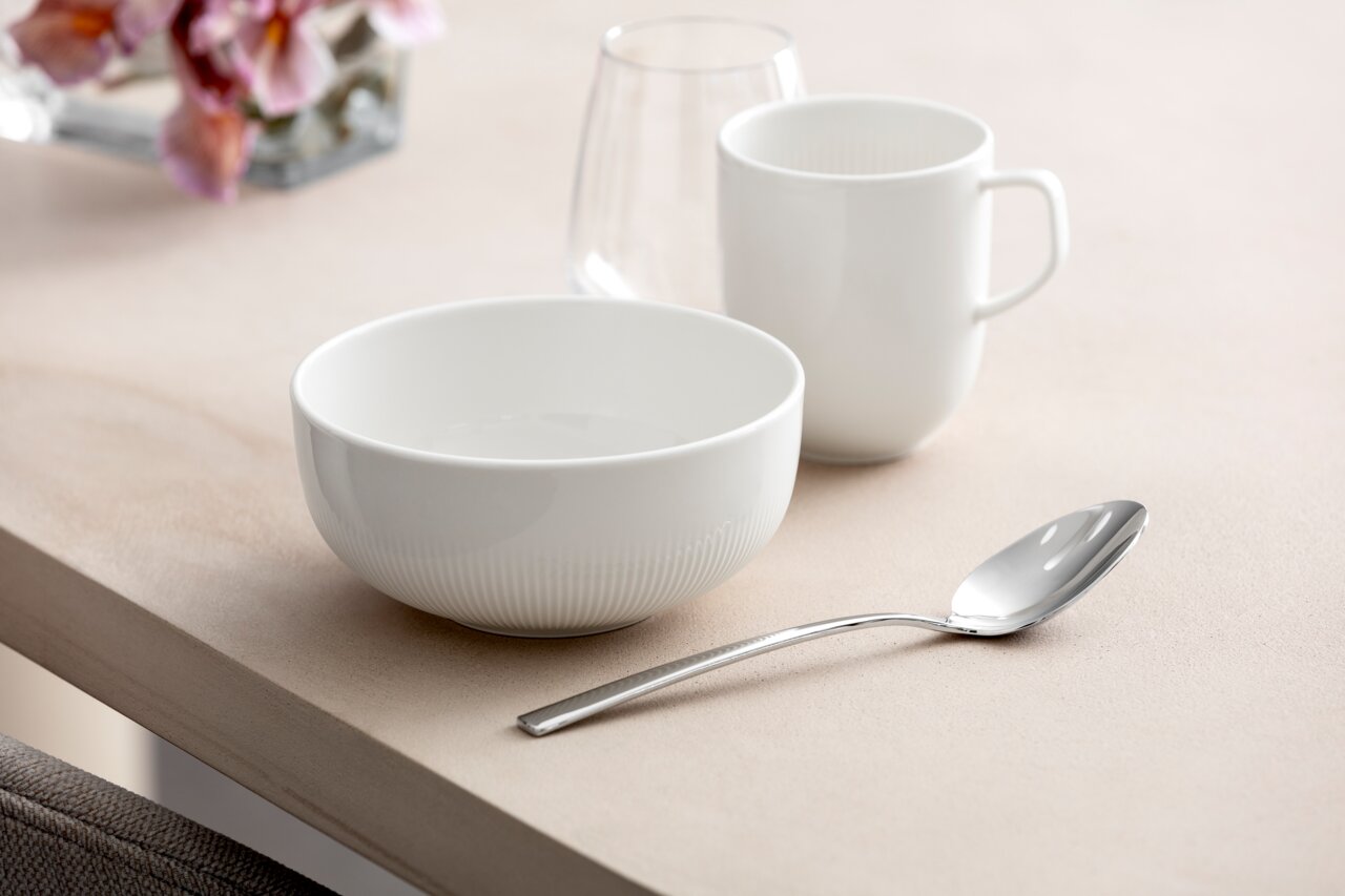 Villeroy & Boch Bowl AFINA Weiße Müslischale Afina 550ml auf einem Tisch, seitliche Perspektive, neben einer Tasse und einem Löffel.