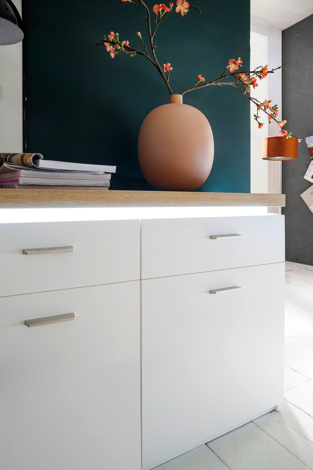 Nahaufnahme eines modernen weißen Sideboards mit Holzoberfläche, dekoriert mit einer großen Vase und Blumen, seitliche Perspektive.
