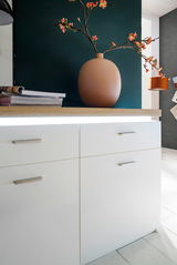 Nahaufnahme eines modernen weißen Sideboards mit Holzoberfläche, dekoriert mit einer großen Vase und Blumen, seitliche Perspektive.