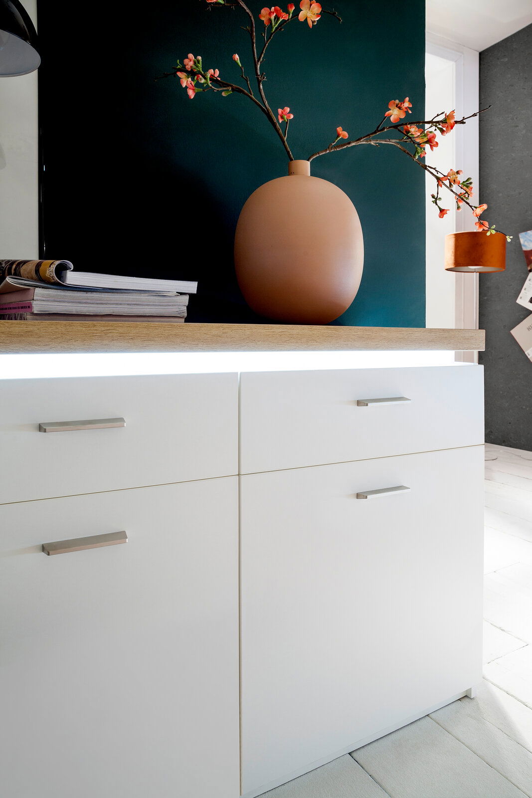 Nahaufnahme eines modernen weißen Sideboards mit Holzoberfläche, dekoriert mit einer großen Vase und Blumen, seitliche Perspektive.