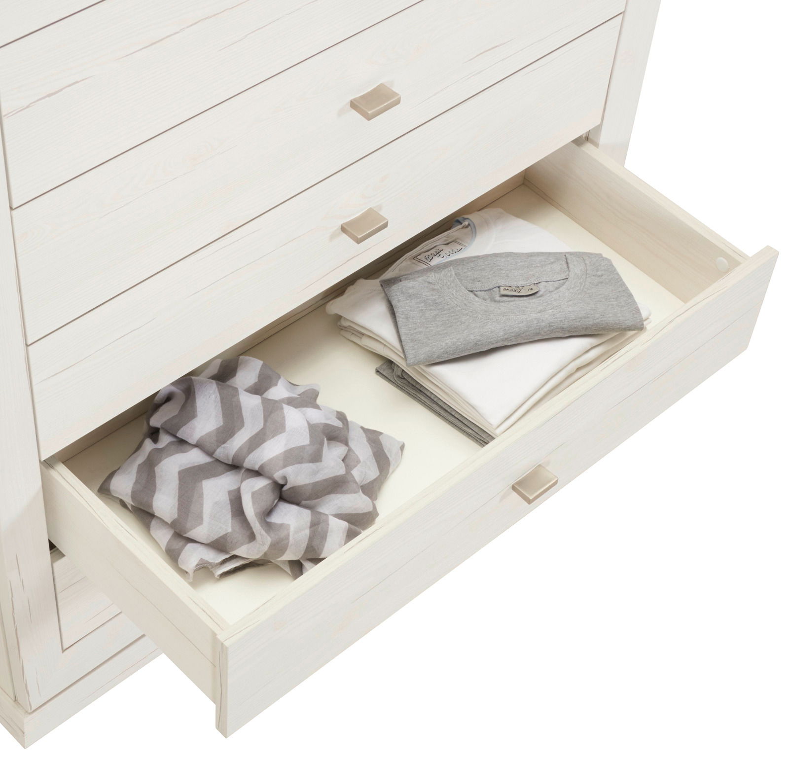 Weiße Kommode CAMRON mit offener Schublade, gefüllt mit gefalteter Kleidung, aus der Vogelperspektive.