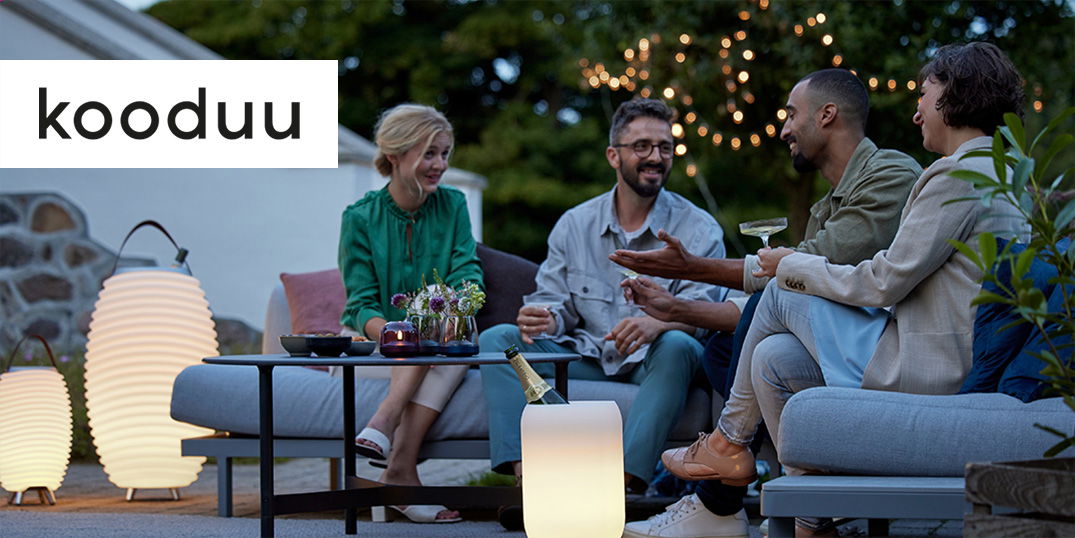 Vier Freunde sitzen bei stimmungsvoller Beleuchtung von Kooduu auf einer Gartenlounge, 