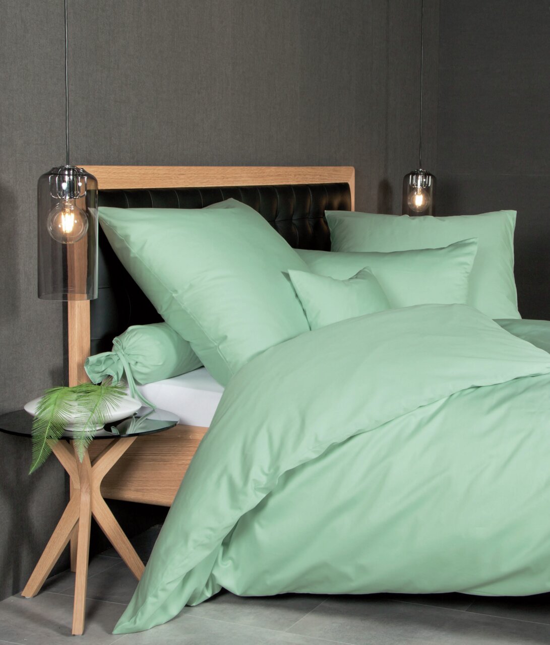 Bett mit mintgrüner Mako-Satin-Bettwäsche, seitliche Perspektive, modernes Design mit Holz- und Lederelementen