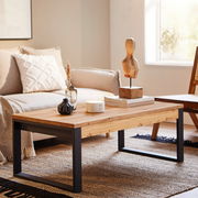 Moderner Couchtisch aus Holz mit schwarzem Metallgestell in einem gemütlichen Wohnzimmer, seitliche Perspektive.