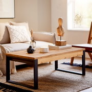 Moderner Couchtisch aus Holz mit schwarzem Metallgestell in einem gemütlichen Wohnzimmer, seitliche Perspektive.