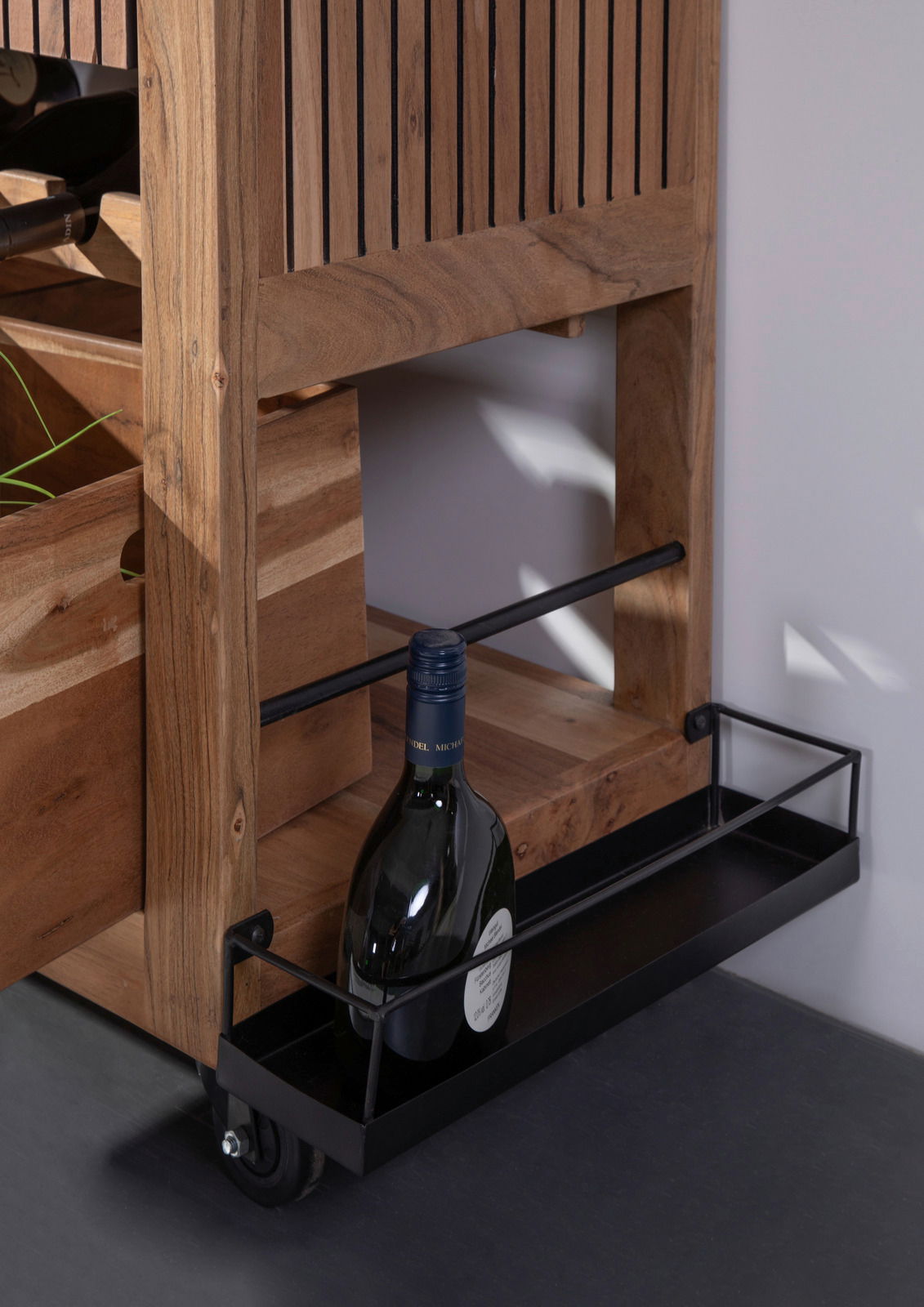 Nahaufnahme eines Servierwagens aus Holz mit einer Flasche Wein in einem unteren Metallregal, seitliche Perspektive.