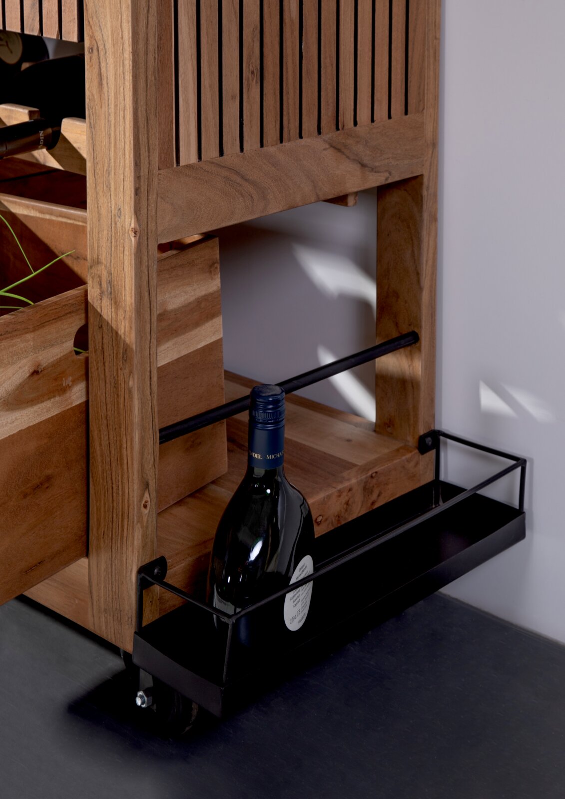 Nahaufnahme eines Servierwagens aus Holz mit einer Flasche Wein in einem unteren Metallregal, seitliche Perspektive.
