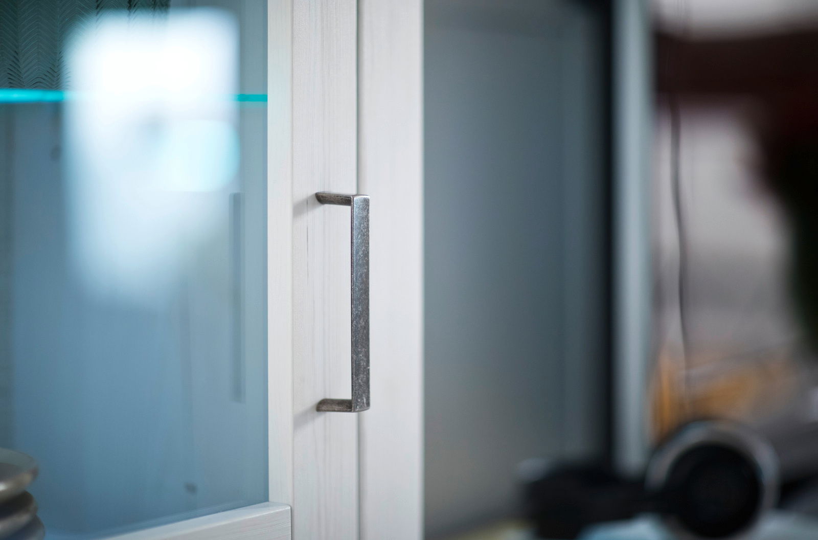 Nahaufnahme eines Schrankgriffs an einer Glastür mit Holzrahmen, seitliche Perspektive
