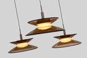 Drie moderne hanglampen met amberkleurige glazen schijven en warm licht, schuin van onderen gezien.