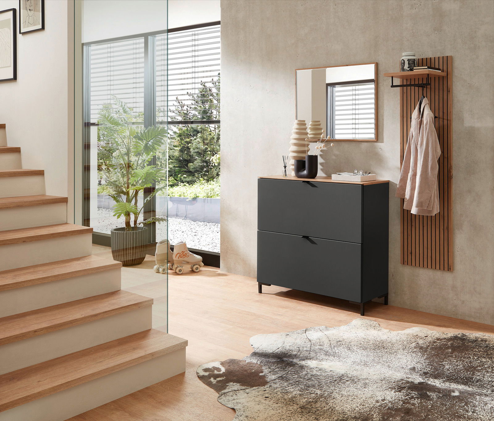 Moderner Eingangsbereich mit einem schwarzen Hänge-Schuhschrank, einem schmalen Spiegel und einem Garderobenpaneel aus Holz. Perspektive von der Seite mit Blick auf die Treppe und den Außenbereich.
