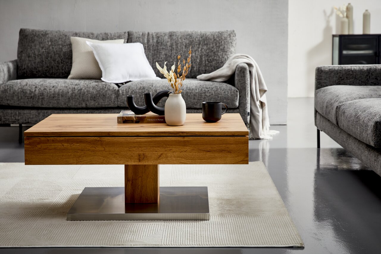 Moderner Couchtisch aus Holz mit Metallfuß, dekoriert mit Vasen und Tassen, in einem stilvollen Wohnzimmer mit grauen Sofas, Frontalansicht.