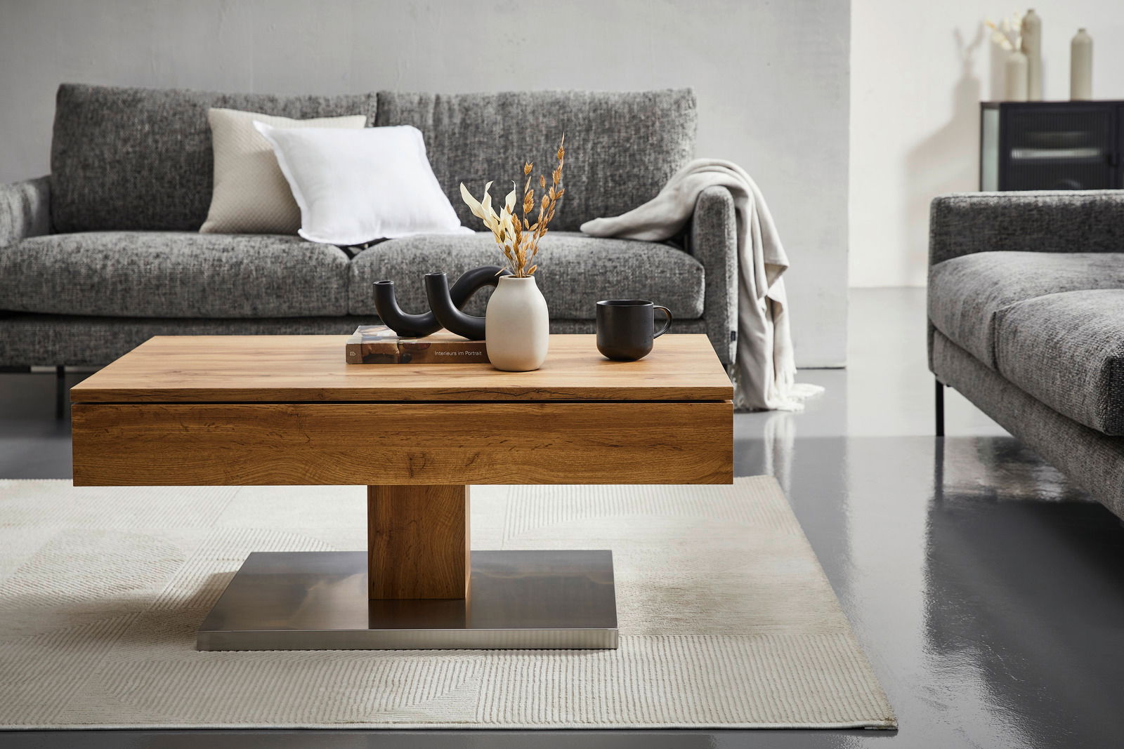 Moderner Couchtisch aus Holz mit Metallfuß, dekoriert mit Vasen und Tassen, in einem stilvollen Wohnzimmer mit grauen Sofas, Frontalansicht.