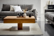 Moderner Couchtisch aus Holz mit Metallfuß, dekoriert mit Vasen und Tassen, in einem stilvollen Wohnzimmer mit grauen Sofas, Frontalansicht.