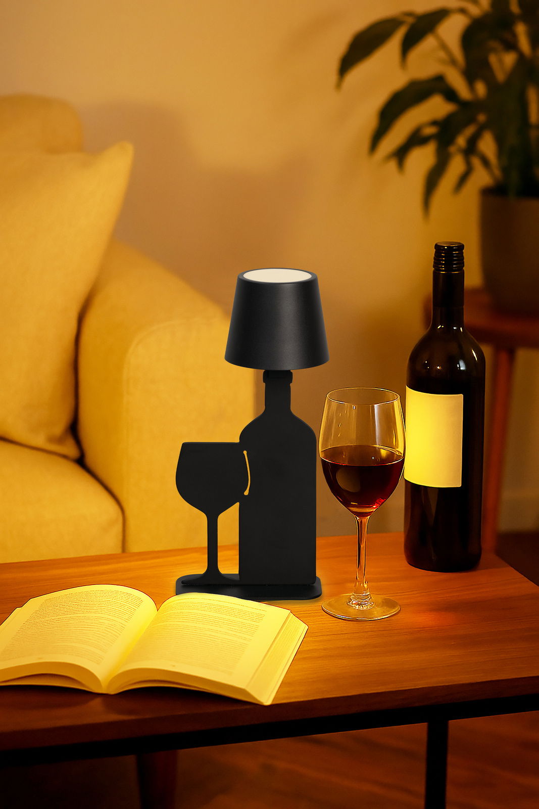 Schwarze Akku-Tischleuchte in Form einer Weinflasche und eines Weinglases, auf einem Tisch neben einem Buch und einem Weinglas, aus seitlicher Perspektive.