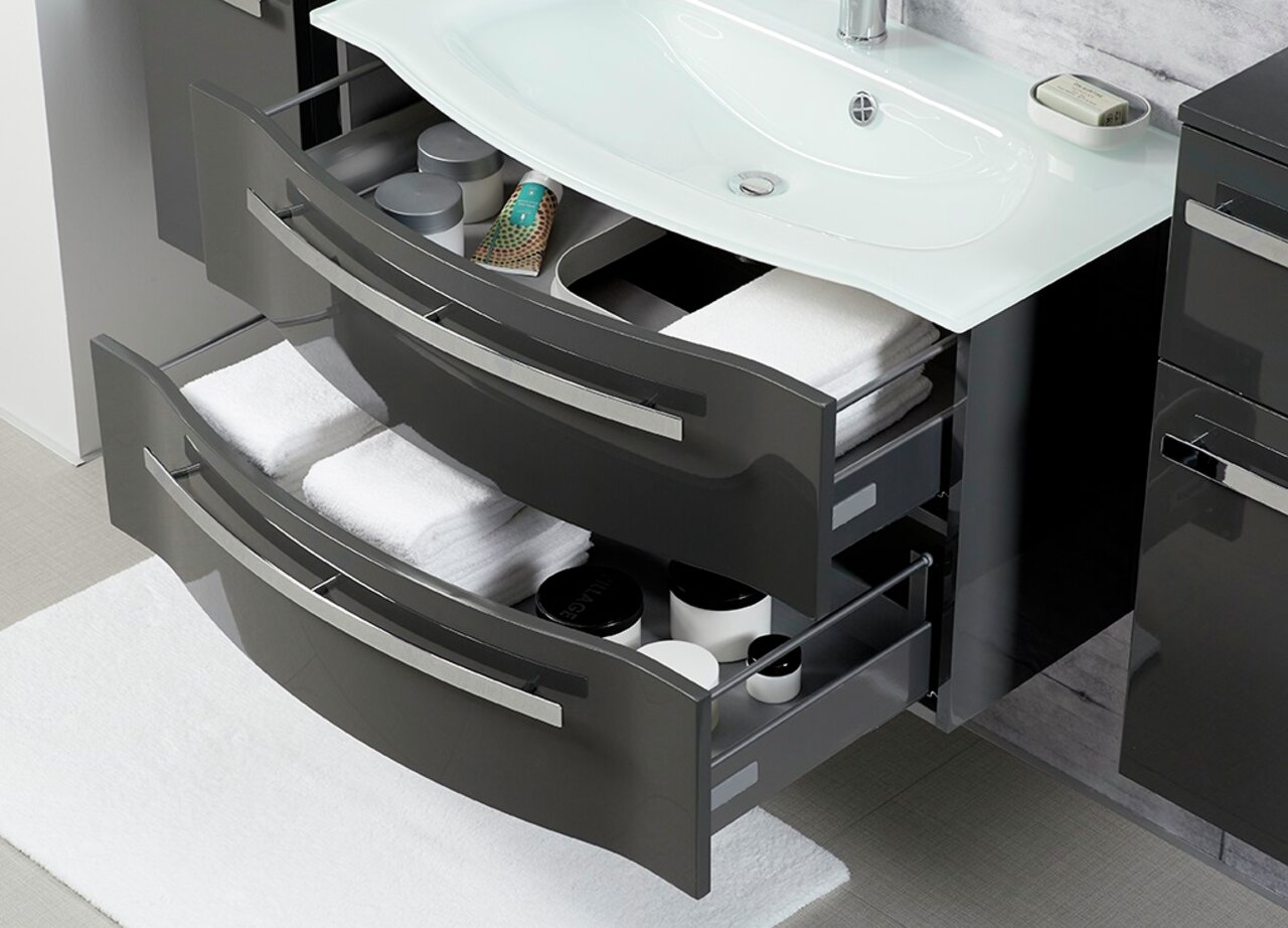 Moderner Badblock mit zwei geöffneten Schubladen, gefüllt mit Handtüchern und Pflegeprodukten, aus der Vogelperspektive fotografiert.