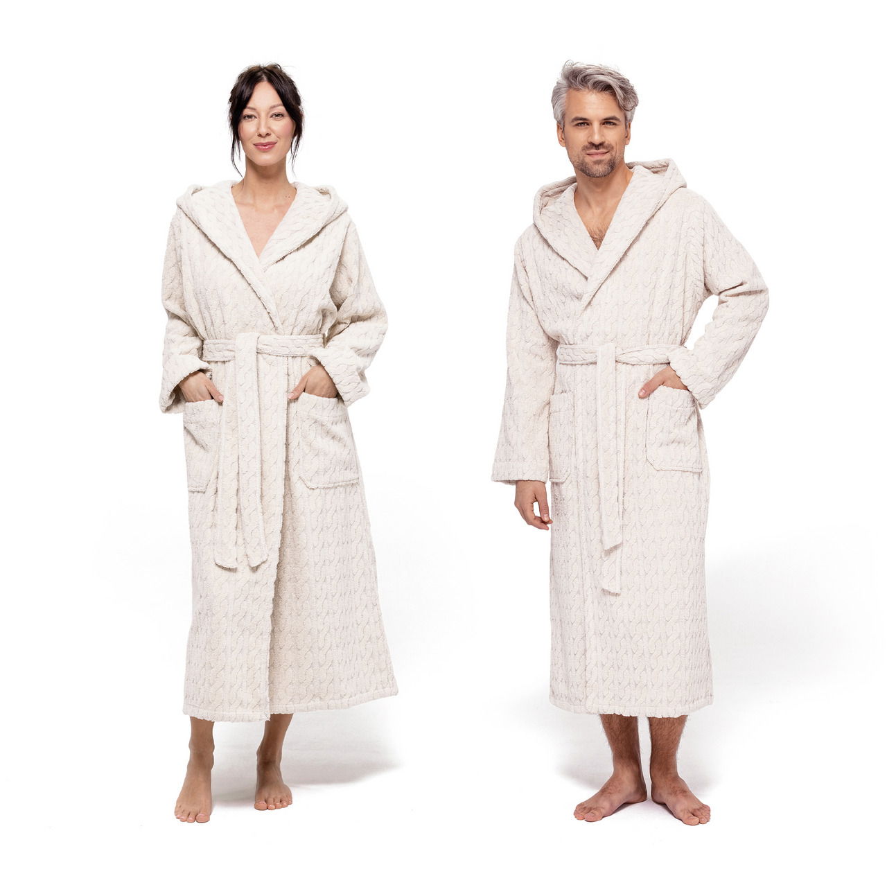 Zwei Personen in cremefarbenen Kapuzenmänteln, frontal fotografiert, mit Taschen und Gürtel.