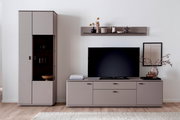 Modernes Wohnzimmer-Setup mit taupefarbener TV-Wohnwand: links hoher Vitrinenschrank mit Glasfach, rechts niedriges TV-Lowboard mit Fernseher und darüber Wandboard mit Deko, frontal aus leichter Schrägperspektive.