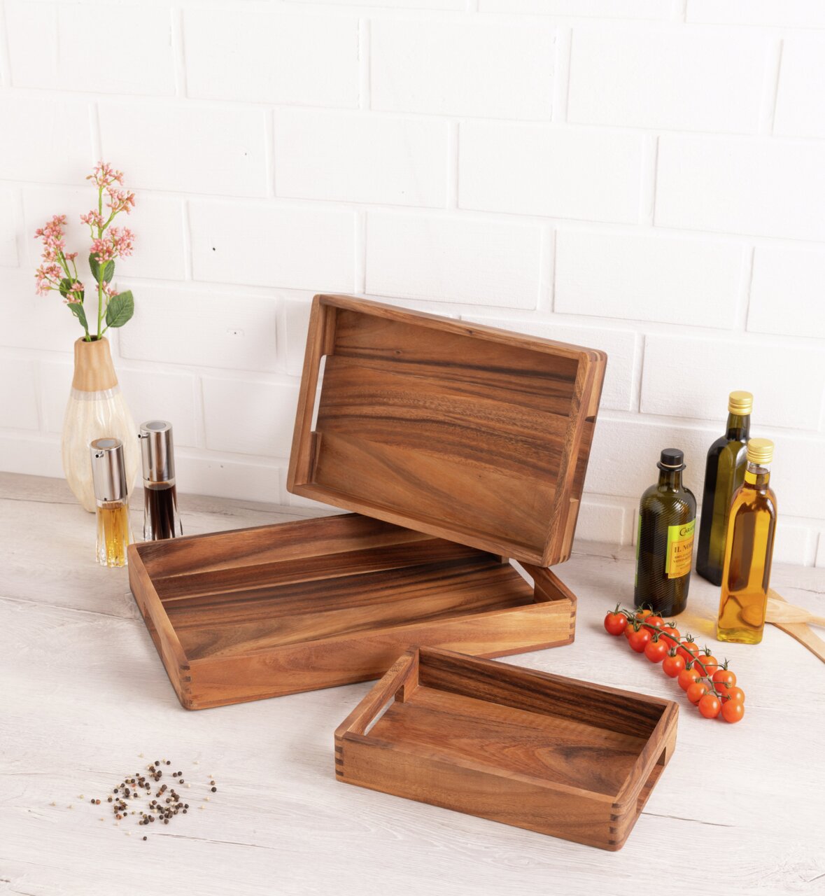 Drei hölzerne Tabletts in verschiedenen Größen, auf einem Tisch arrangiert, mit einer dekorativen Vase und Gewürzflaschen im Hintergrund. Perspektive von oben.
