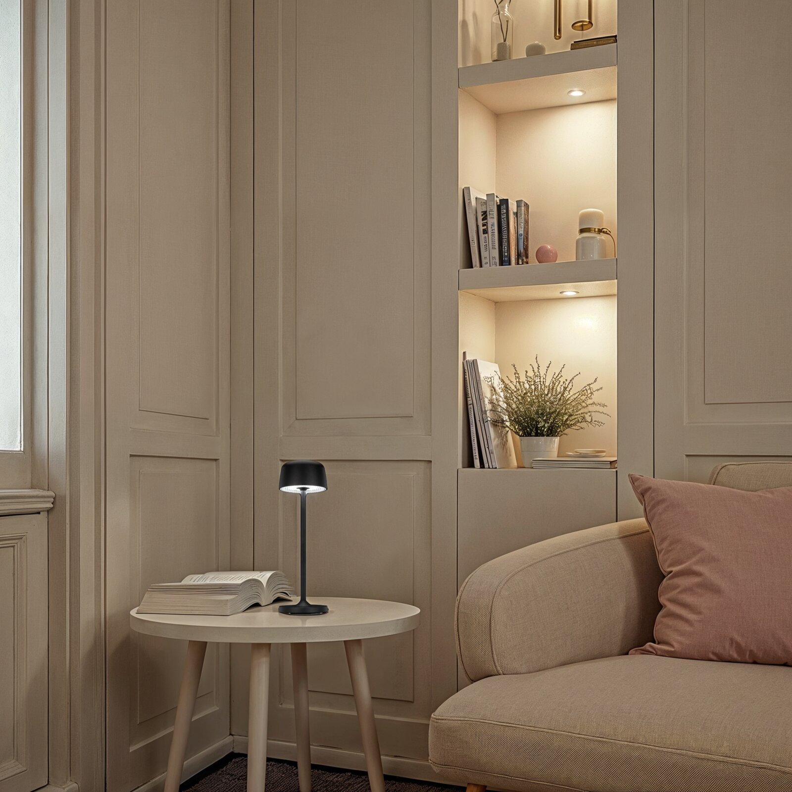 Schwarze, moderne Tischleuchte mit warmweißem Licht auf rundem Beistelltisch neben beigem Sofa, seitliche Perspektive im Wohnzimmer