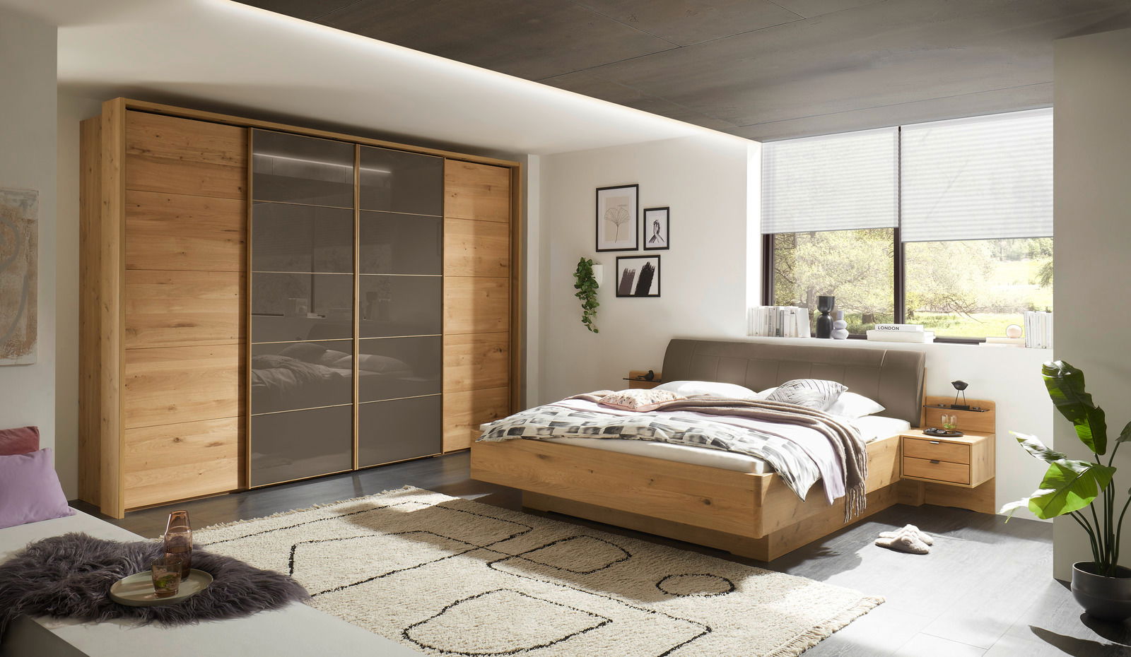 Moderner Schwebetürenschrank mit vier Türen in Holzoptik und grauen Glaselementen, seitliche Perspektive im Schlafzimmer.