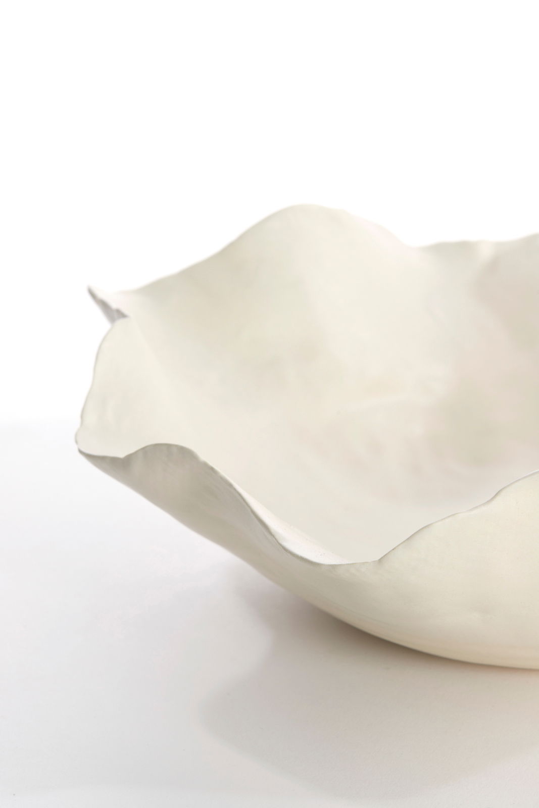 Nahaufnahme einer weißen, organisch geformten Schale mit unregelmäßigem Rand, seitliche Perspektive.