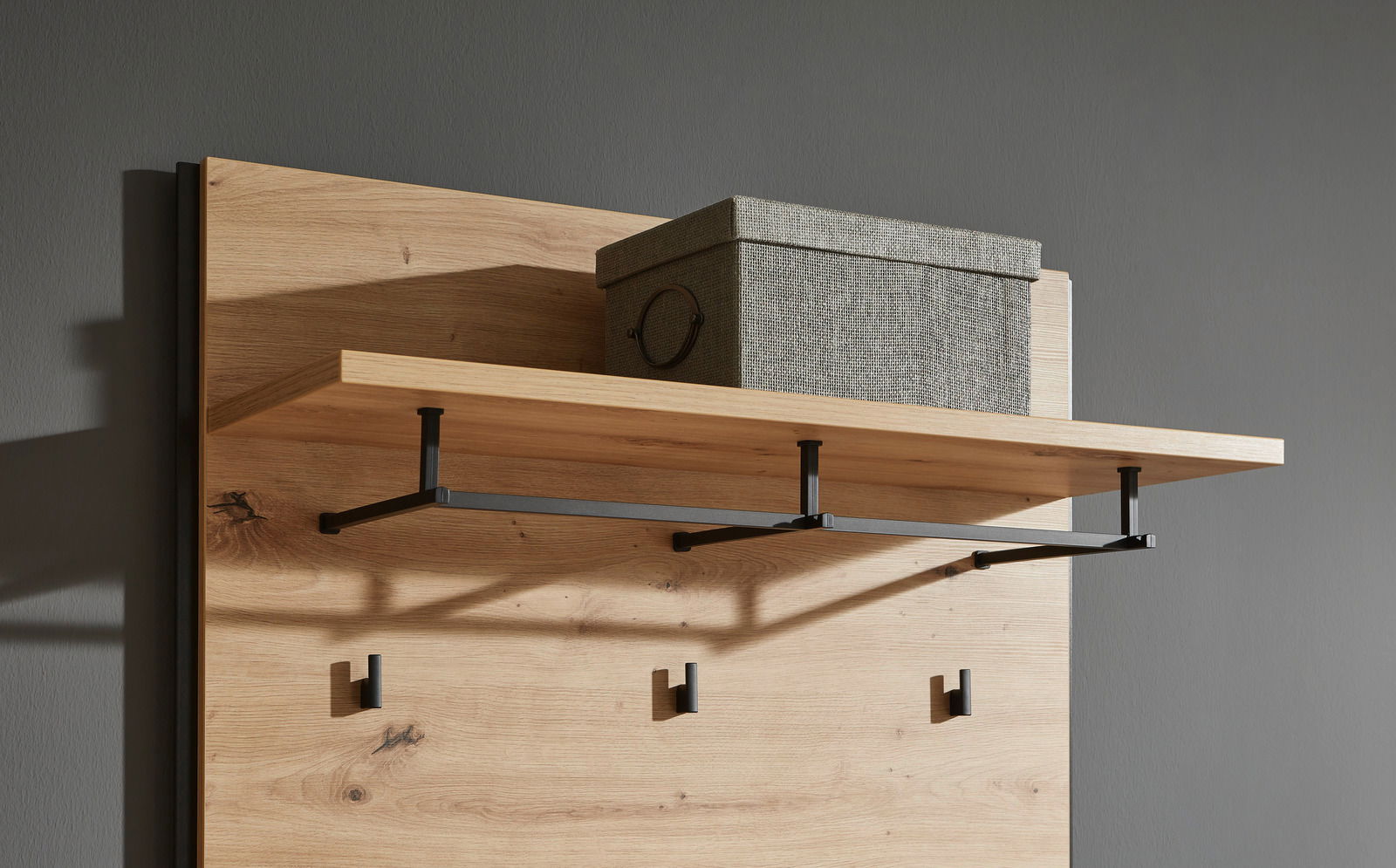 Garderobenpaneel aus Holz mit schwarzem Metallgestell, seitliche Perspektive. Oben befindet sich ein Regalbrett mit einer grauen Aufbewahrungsbox.