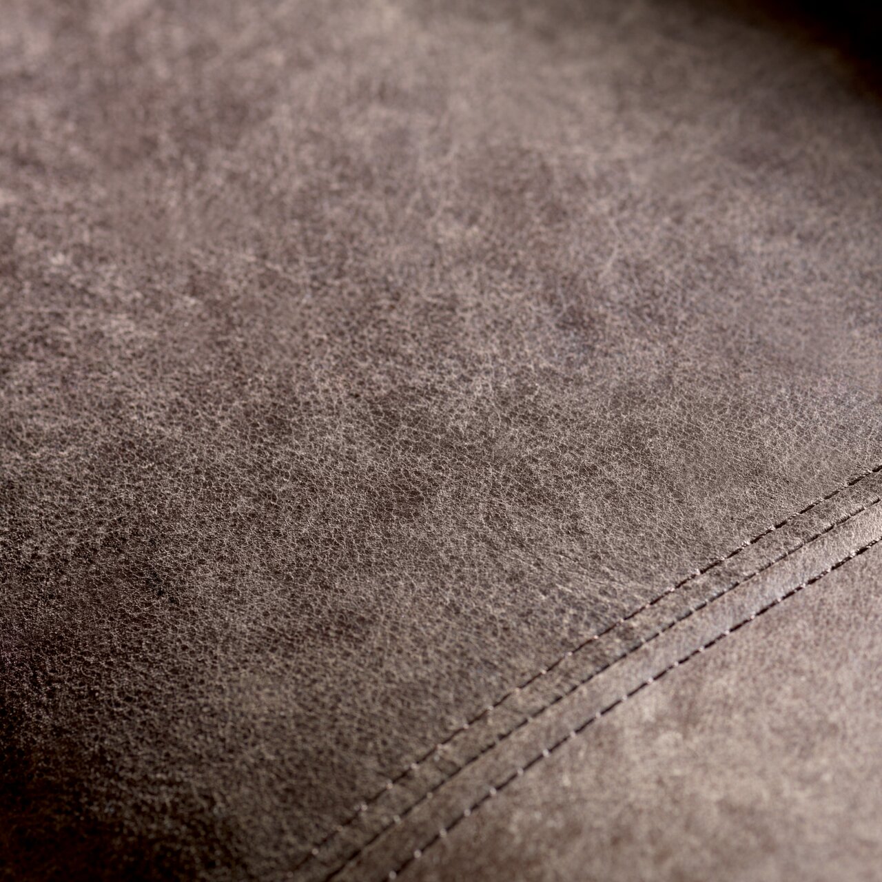 Nahaufnahme der Textur eines braunen Ledersofas mit sichtbaren Nähten, von oben betrachtet.
