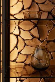 Nahaufnahme eines Regals mit dekorativem Kaminholz-Rückwandakzent und Glasvasen, seitliche Perspektive.