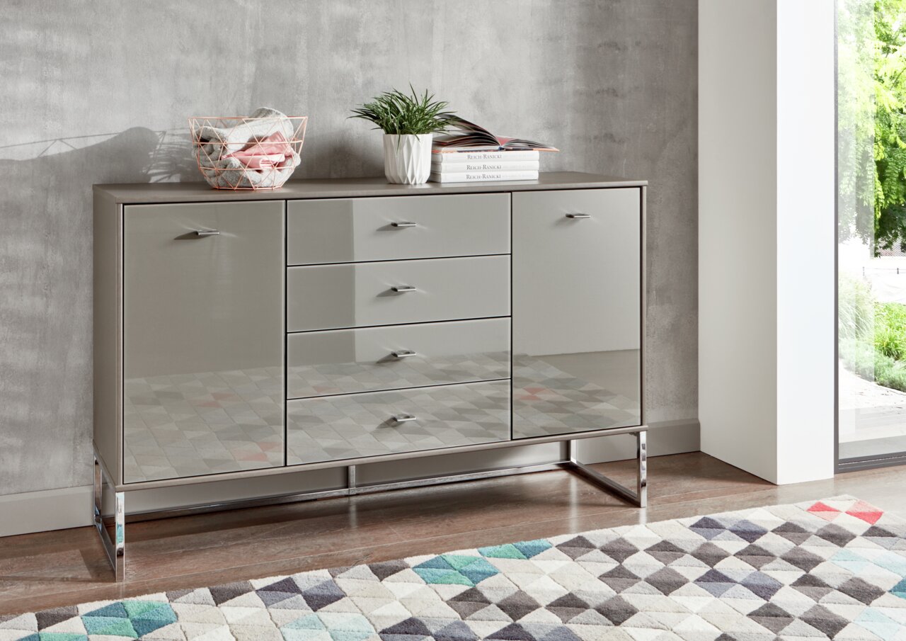 Moderne Kombikommode mit glänzenden Fronten, seitlicher Perspektive, dekoriert mit Pflanzen und Büchern.