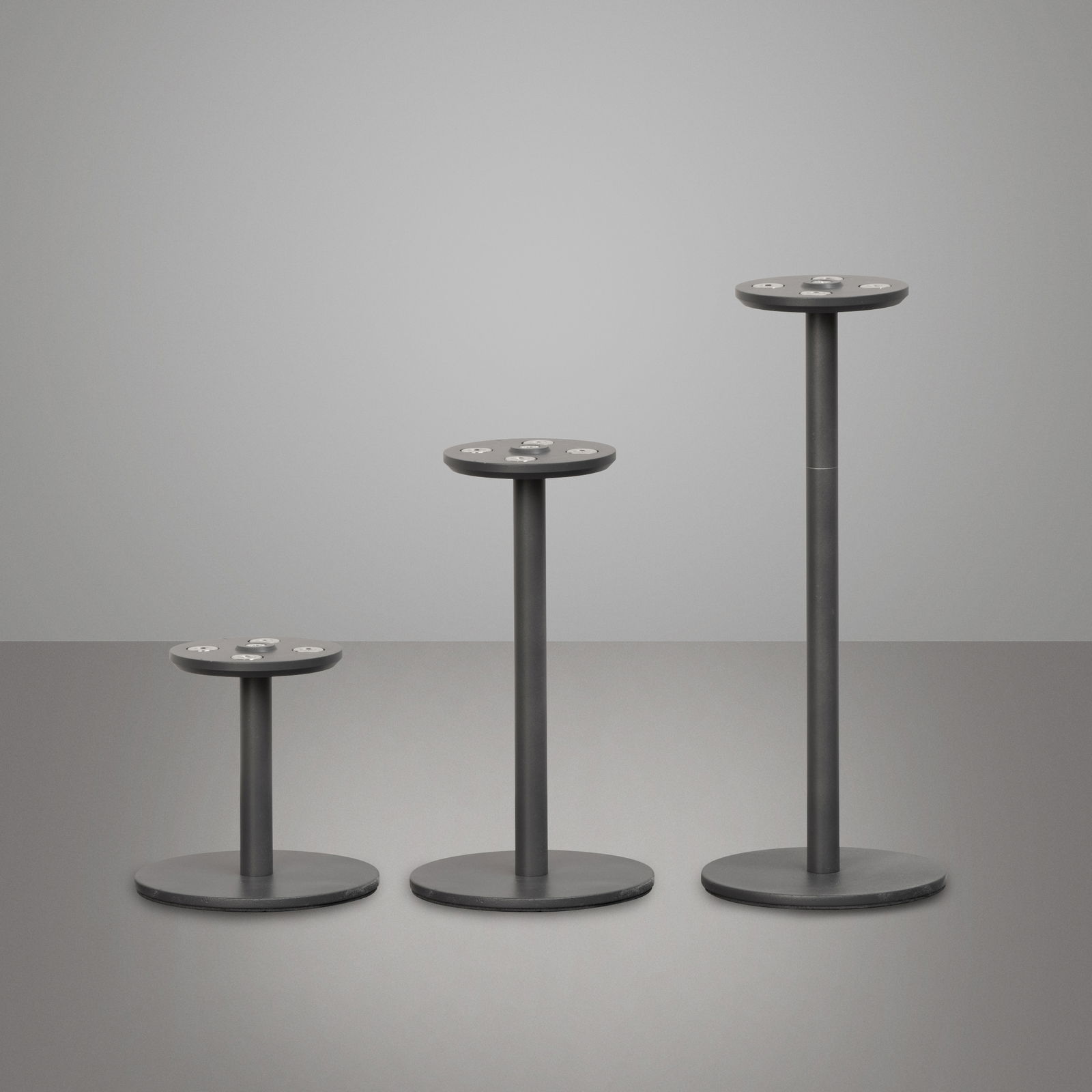 Drei unterschiedlich hohe, schwarze Gestelle für Akku-Windlichter, frontal betrachtet auf grauem Hintergrund.