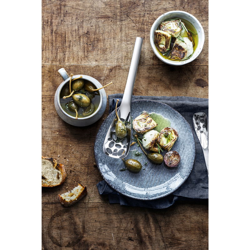 Vogelperspektive auf einen Servierlöffel Nuova 25cm auf einem gedeckten Tisch mit Oliven und Artischocken.