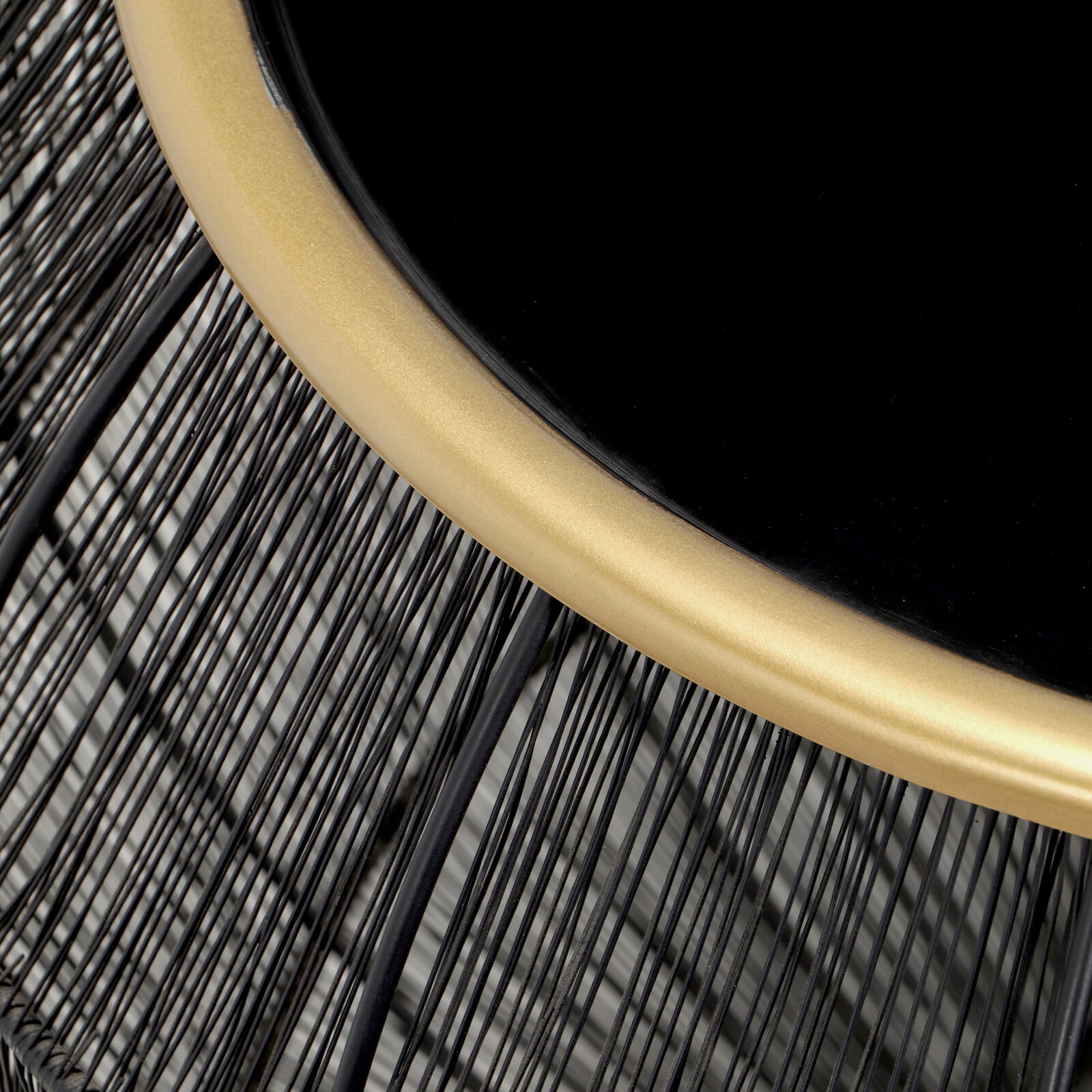 Nahaufnahme eines Beistelltisches mit schwarzer Tischplatte und goldfarbenem Rand, Drahtgestell aus schwarzem Metall, von oben betrachtet.