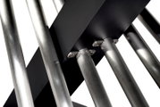 Detailaufnahme aus der Untersicht auf gebürstete Edelstahlrohre mit verschraubten Halterungen an schwarzen Metallplatten