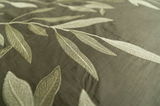 Nahaufnahme von Bettwäsche mit gesticktem Blattmuster in Grün- und Beigetönen, von oben betrachtet.